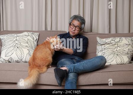 Der ältere asiatische Mann sitzt auf dem Sofa im Wohnzimmer. Stockfoto