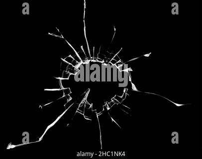 Struktur von Rissen am Fenster, gebrochenes Glas mit einem Loch auf schwarzem Hintergrund Stockfoto