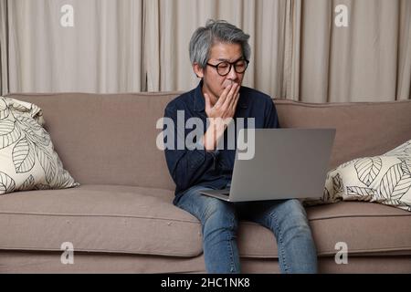 Der ältere asiatische Mann sitzt auf dem Sofa im Wohnzimmer. Stockfoto