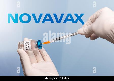 Turin, Italien - 18. Dezember 2021: Krankenschwesternhände mit Latexhandschuhen und einer Spritze, die den Impfstoff aus dem Fläschchen nimmt, im Hintergrund Novavax Laboratory Logo Stockfoto