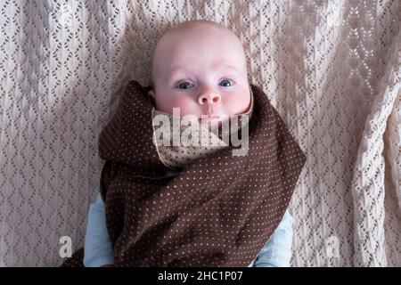 Niedliches Baby mit großen blauen Augen, das einen Hut und einen riesigen Strickschal trägt Stockfoto