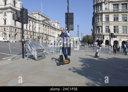 London, England, Großbritannien. Männer fahren auf dem Bürgersteig auf dem Parliament Square mit E-Scootern Stockfoto