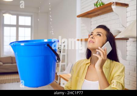 Eine junge Frau ruft wegen einer beschädigten und undichten Decke in ihrem Haus den Reparaturdienst an Stockfoto