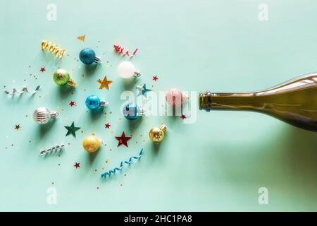 Feuerwerk aus einer Flasche Champagner und Konfetti und weihnachtsbaumschmuck auf grünem Hintergrund glücklicher Weihnachtsurlaub im neuen Jahr Stockfoto