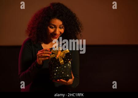 Glückliche junge Frau, die überrascht beim Auspacken der Geschenkbox aussieht Stockfoto