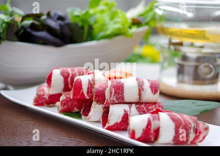 Geschnittene rohe Rinderrollen für heißen Topf auf weißem Teller Stockfoto