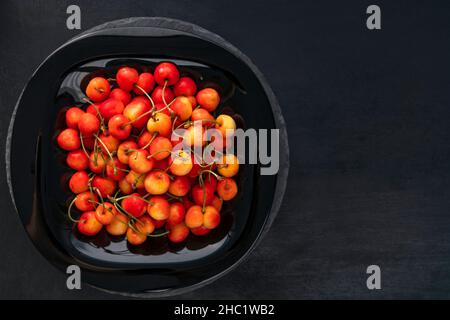 Reife Kirschen in Teller auf schwarzem Hintergrund Draufsicht. Süße, saftige Kirschen. Draufsicht, Kopierbereich. Stockfoto