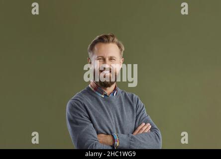 Porträt eines gutaussehenden lächelnden bärtigen Mannes, der auf grünem Hintergrund mit gefalteten Armen steht. Stockfoto