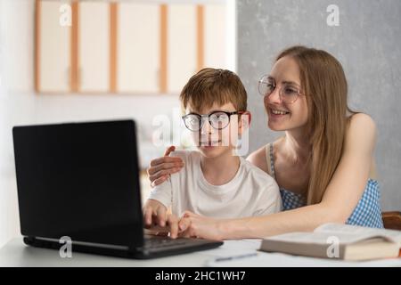 Mutter und Sohn machen Hausaufgaben am Computer. Schwester hilft ihrem Bruder beim Unterricht. Tutor erklärt dem Kind das Thema Stockfoto