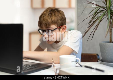 Teenager ist in der Programmierung beschäftigt. Kind mit Brille starrt aufmerksam auf den Laptop-Monitor. Homeschool . Stockfoto