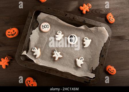 Kürbis- und Geisterkeks in weiß und orange auf dem Tisch und in einer Backform. Draufsicht auf dem Tisch. Stockfoto