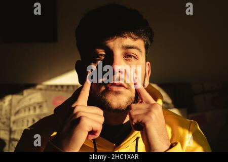 Ein junger gutaussehender hispanischer Mann mit einem gelben Hoodie, der unter dem hellen Sonnenlicht der goldenen Stunde posiert Stockfoto