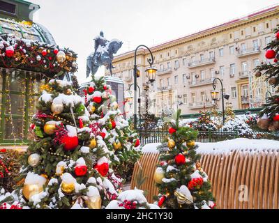 Moskau. Russland. 23. Dezember 2021. Bunte Dekorationen und Kugeln auf den Bäumen des Neujahrs auf der Straße in Moskau. Weihnachtsbäume mit Schnee bedeckt in der Nähe des Denkmals für Juri Dolgoruky. Selektiver Fokus. Stockfoto