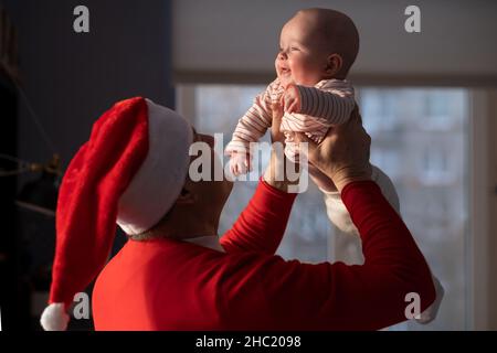 Kaukasischer Großvater in rotem Hut spielt mit Enkelin zu Hause selebrating Weihnachten Stockfoto
