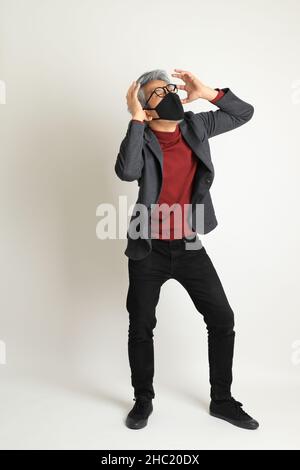 Der ältere asiatische Mann im eleganten Casual auf dem weißen Hintergrund stehend. Stockfoto