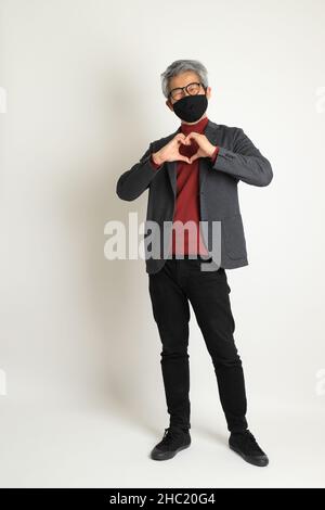 Der ältere asiatische Mann im eleganten Casual auf dem weißen Hintergrund stehend. Stockfoto