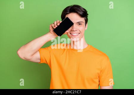 Foto von fröhlichen jungen glücklichen Mann decken Auge Gesicht Telefon leeren Raum Lächeln isoliert auf grünem Hintergrund Stockfoto