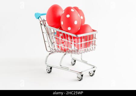 Dekorative rote Ostereier in einem kleinen Supermarkt-Einkaufswagen isoliert auf einem weißen Tisch Stockfoto