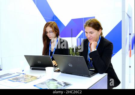 Zwei lächelnde Büroangestellte sitzen vor Laptops und arbeiten. Ausstellung Waffen und Sicherheit-2018 . 12. Oktober 2018. Kiew, Ukraine Stockfoto