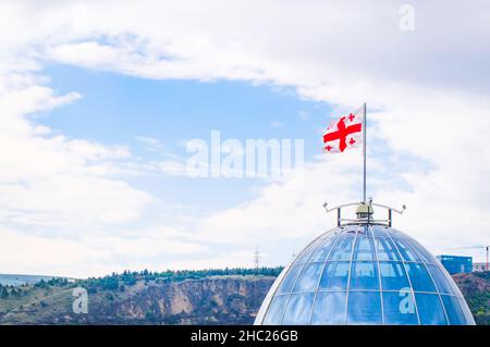 Panoramaansicht des Präsidentenpalastes oben Glaskuppel mit georgischer Flagge, Frühling Natur und Berge im Hintergrund. Konzept der georgischen Politik und