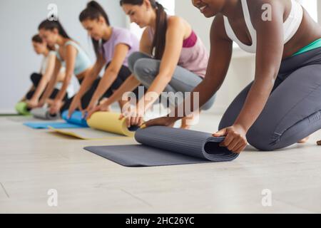 Eine Gruppe glücklicher Mädchen rollt nach dem Yoga-Training oder dem Fitnesstraining im Fitnessstudio Gummimatten auf Stockfoto