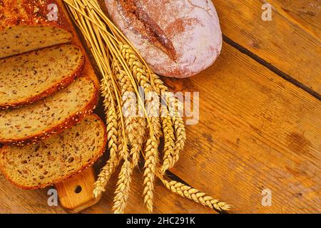 Brotlappen, Brotscheiben und Ähren auf Holzhintergrund. Rustikales und ländliches Konzept. Speicherplatz kopieren. Stockfoto