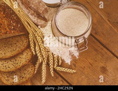 Brotlappen, Brotscheiben, Weizenmehl und Ähren auf Holzhintergrund. Rustikales und ländliches Konzept. Nahaufnahme. Flach liegend. Speicherplatz kopieren. Stockfoto