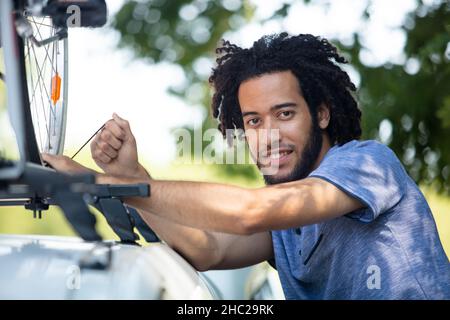 Männlicher Radfahrer, der mit dem Mountainbike vom Gepäckträger auf das Auto fährt Stockfoto