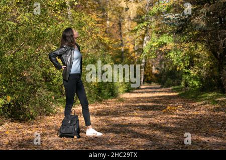 Einsame junge Frau mit dunklem Haar, die im Wald ruht und warmes Wetter genießt. Mädchen geht im Freien, sonnigen Park Stockfoto