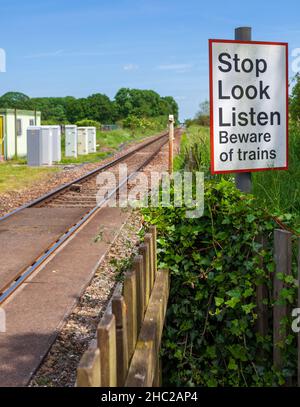 Blick auf eine Haltestelle Hören Sie sich das Bahnschild neben einem Bahnübergang über eine eingleisige Eisenbahnlinie in Yorkshire an Stockfoto