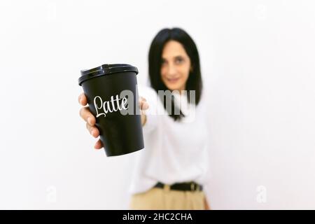 Nahaufnahme der schwarzen Einweg-Kaffeetasse mit Latte-Titel darauf von einer jungen Frau im Hintergrund gehalten. Konzept der Kaffeeindustrie und des Geschäfts. Leer Stockfoto
