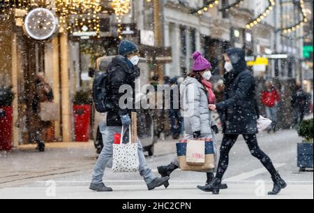 Hamburg, Deutschland. 23rd Dez 2021. Passanten laufen am Vorweihnachtstag mit Einkaufstaschen durch die Innenstadt bei leichtem Schneefall. Quelle: Markus Scholz/dpa/Alamy Live News Stockfoto