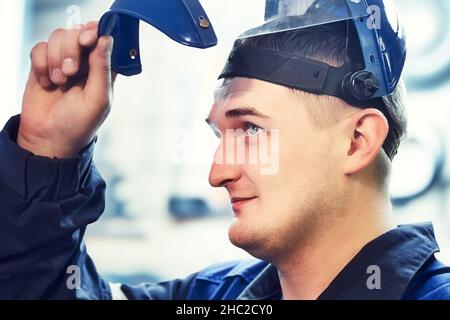 Porträt eines Metallarbeiters oder Arbeiters. Junge Kaukasierin sieht unter dem Visier der Schutzmaske aus. Echter Arbeiter in der Werkstatt. Nahaufnahme. Gesicht im Hochformat. Stockfoto