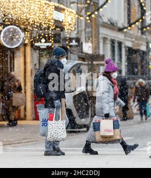 Hamburg, Deutschland. 23rd Dez 2021. Passanten laufen am Vorweihnachtstag mit Einkaufstaschen durch die Innenstadt bei leichtem Schneefall. Quelle: Markus Scholz/dpa/Alamy Live News Stockfoto