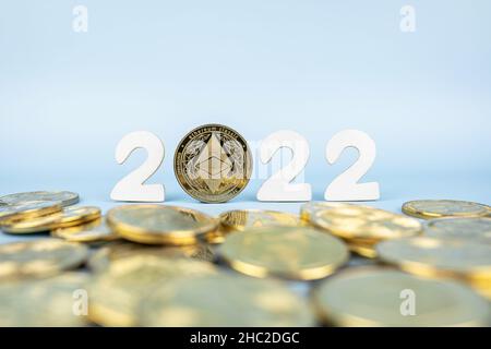 Ethereum 2022 Preisvorhersage-Konzept. Äthermünze, die neben Kryptowährungstoken und Jahreszahlen auf blauem Hintergrund steht. Nahaufnahme, Weichfokus. Stockfoto