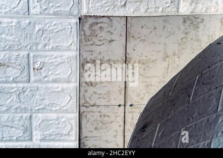 Die Tapete beginnt sich abzulösen. Die Tapete aus alten weißen Ziegeln schälte sich von der Wand im Raum, weil es feucht war oder sich nicht gut klebte. Reparieren Sie A Stockfoto