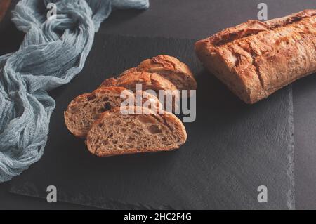 Handgemachtes französisches Brot Selection Baguette mit grauer Gaze-Tischdecke auf schwarzem Hintergrund Stockfoto