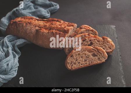 Handgemachtes französisches Brot Selection Baguette mit grauer Gaze-Tischdecke auf schwarzem Hintergrund Stockfoto