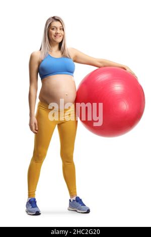 Ganzkörperportrait einer Schwangeren mit einem Crop Top und Leggings, die einen Fitnessball auf weißem Hintergrund isoliert halten Stockfoto