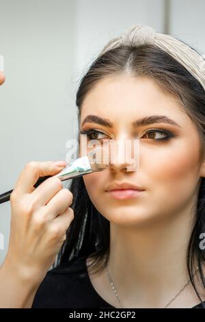 Nahaufnahme Porträt einer Frau, die trockene kosmetische tonale Grundlage auf das Gesicht mit einem Make-up-Pinsel. Make-up-Details Stockfoto