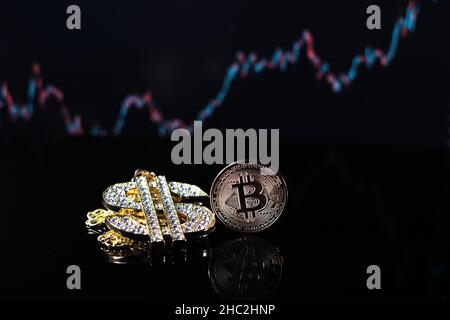 Eine Bitcoin-Münze liegt neben einem mit Diamanten besetzten Anhänger der Dollarkette Stockfoto