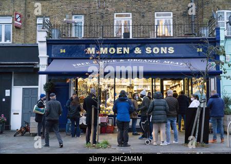 London, Großbritannien, 23. Dezember 2021: Kunden stehen vor der lokalen Metzgerei Moen and Sons in der Altstadt von Clapham. Kunden, die Truthähne, Gänse oder Enten zu Weihnachten sammeln, standen auf einer Seite in der Schlange. Diejenigen, die Fleisch, Käse und Delikatessen kaufen wollten, standen auf der anderen Seite in der Schlange. Anna Watson/Alamy Live News Stockfoto