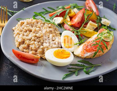 Frühstück Haferbrei Haferbrei mit gekochtem Ei, Lachs Sandwich und Tomaten Salat. Gesunde Ernährung. Stockfoto