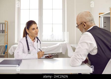 Junge Ärztin, die während eines Termins in der Klinik ihrem älteren männlichen Patienten zuhört Stockfoto