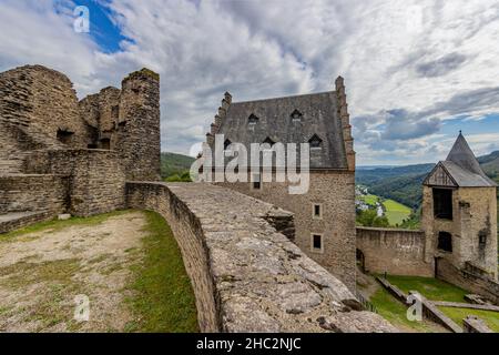 Oberer Innenhof in den Außenruinen der mittelalterlichen Burg Bourscheid, zerstörte Mauern, ein Gebäude und der Wachturm, Hügel mit üppigem Grün bedeckt Stockfoto