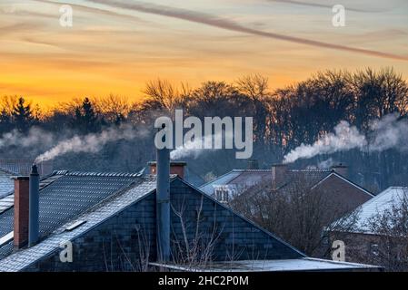 Rauchender Hausdachkamin aus Häusern, die Dampf/Dampf aus Gaskesseln zur Zentralheizung bei Sonnenaufgang an eiskaltem Wintermorgen abgeben Stockfoto