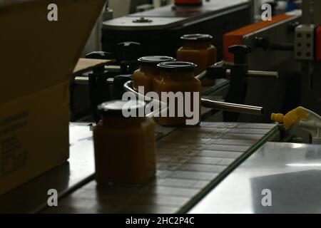 Gläser mit Rahmhonig in einer Verpackungslinie in einer kommerziellen Honigfabrik Stockfoto