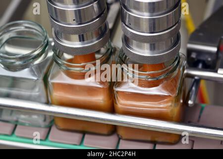 Gläser mit Rahmhonig in einer Verpackungslinie in einer kommerziellen Honigfabrik Stockfoto