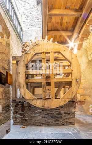 Vianden, Luxemburg. 25. September 2021. Rekonstruiertes Holzrad, um Wasser im Inneren der Burg zu Pumpen, zwischen Steinmauern in einem kleinen Raum beleuchtet w Stockfoto