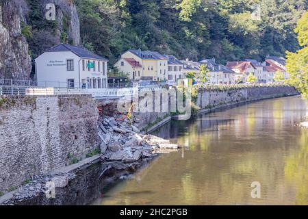 Vianden, Luxemburg. 25. September 2021.Ziegelmauer mit einem Teil von einem großen Sturm auf dem Fluss Our mit Häusern auf einem Berghang im Hintergrund gebrochen, Stockfoto